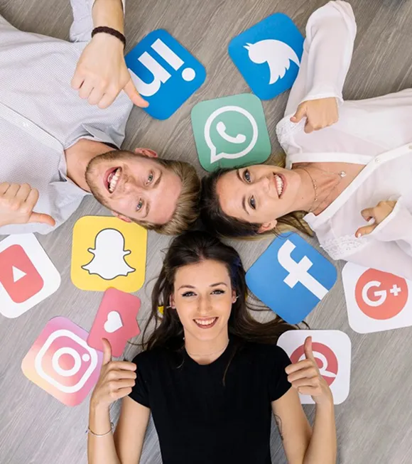 Three people lying on the floor surrounded by various social media icons, engaging in a relaxed, collaborative atmosphere.